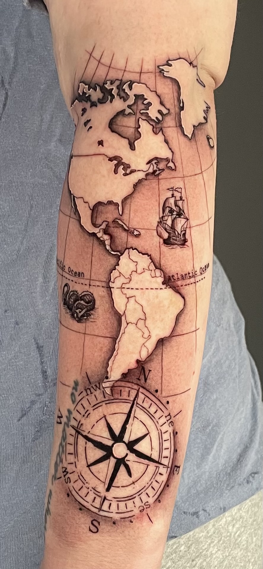 Black and grey world map and compass forearm tattoo by Chandler Neshan