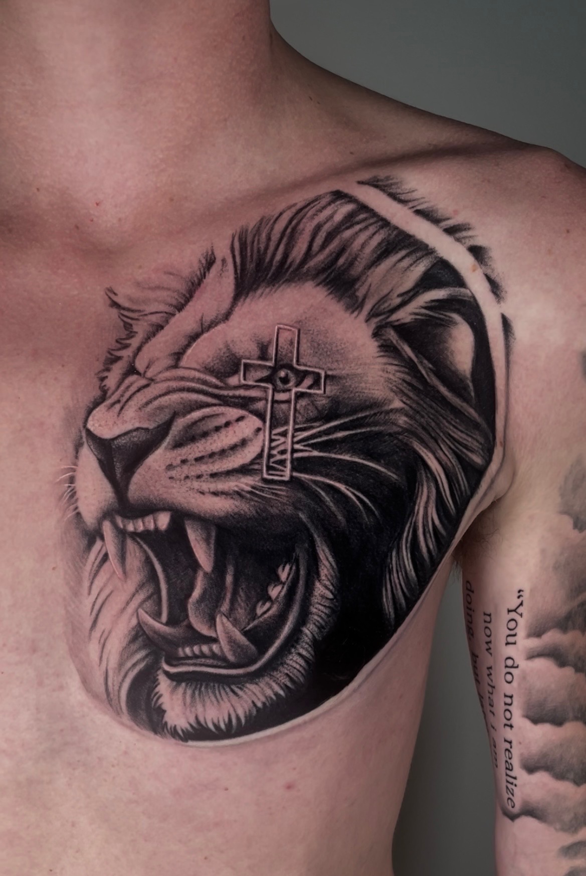 Black and grey roaring lion with cross chest tattoo by Chandler Neshan